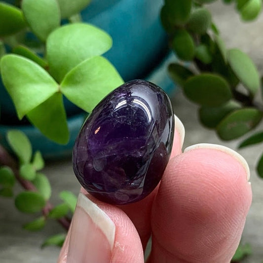 Shimmering purple amethyst egg with intricate patterns and a sense of mystique held delicately by the tips of three fingers
