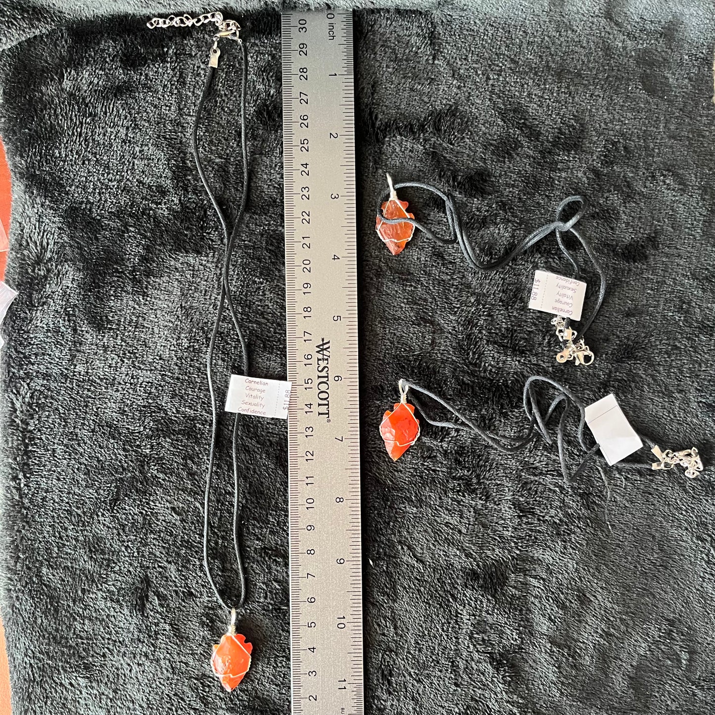 3, 1 inch vibrant orange raw carnelian agate arrowhead, handmade, wire wrapped necklaces, attatched to a 20 inch asjustable black cord, lying next to a ruler