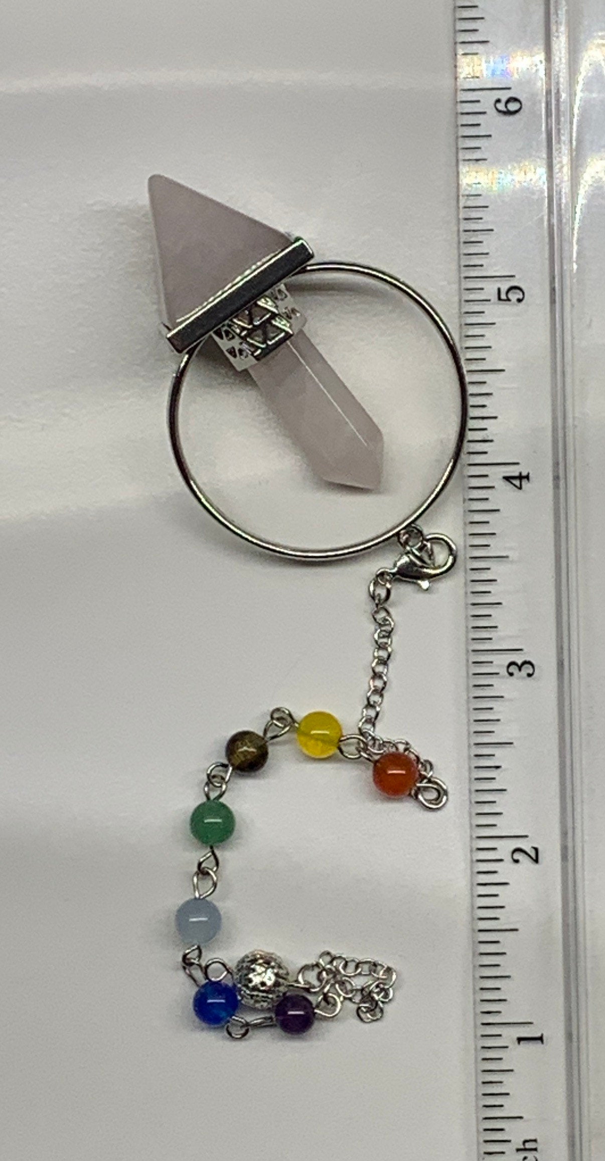 2 in pendulum including rose quartz inverted pyramid attached to rose quartz crystal point in a silver hoop, connected to an 8 inch chain including chakra beads displayed next to a ruler.