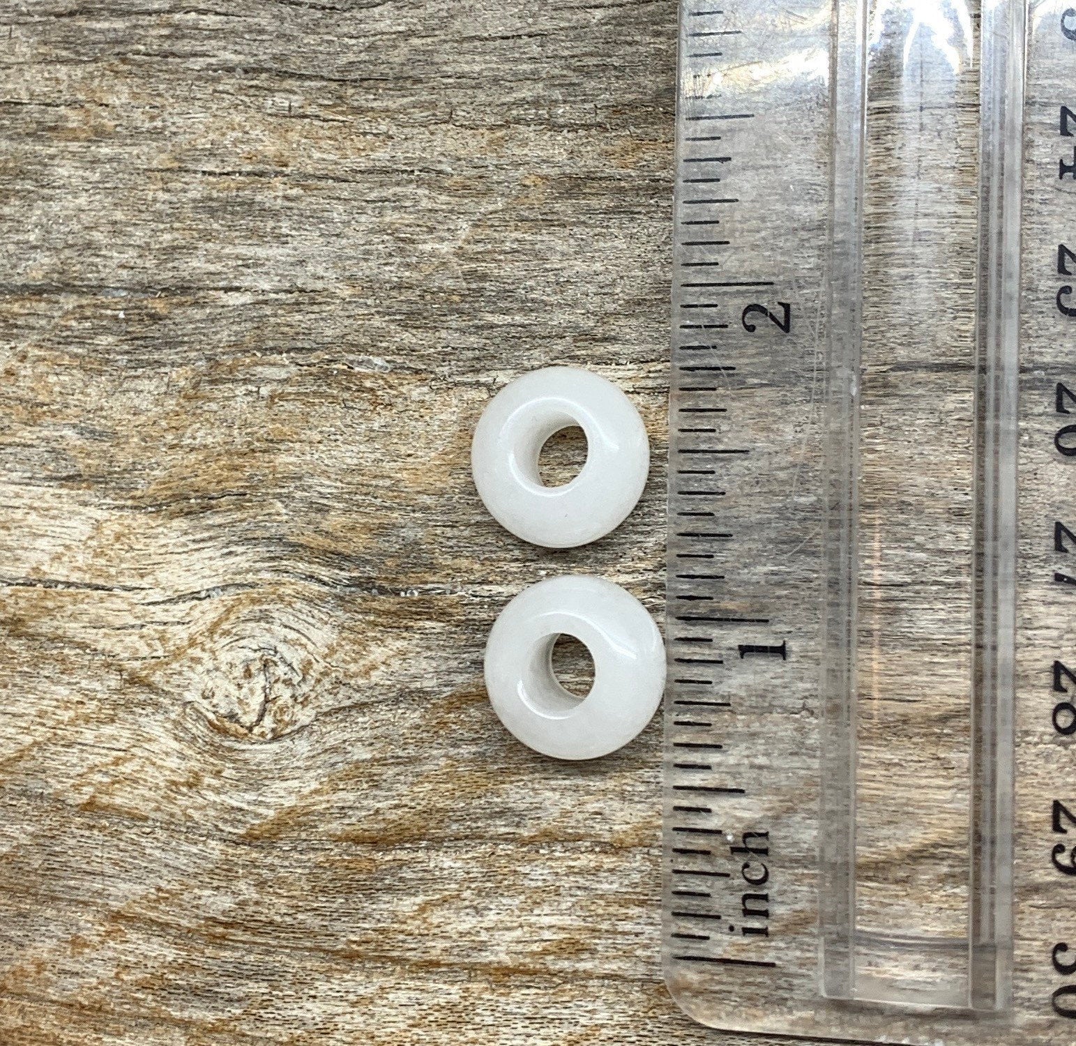 "Close-up of 14mm snow quartz crystal beads, showcasing their translucent white color and smooth surface texture, positioned next to a ruler