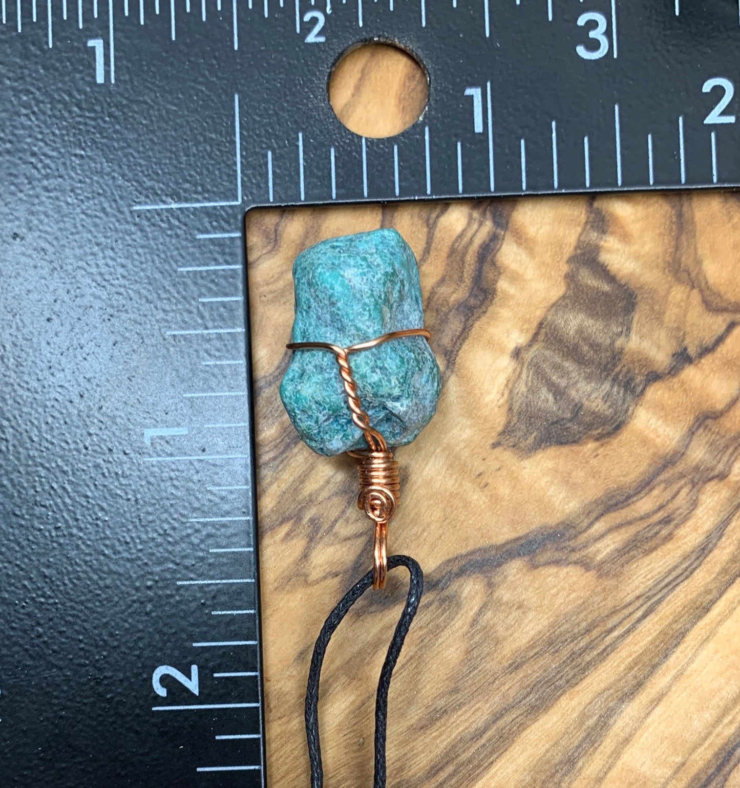 Copper wire wrapped turquoise nugget pendant, approximately 1" long, attatched to an asjistable black cord, dosplayed next ro a ruler