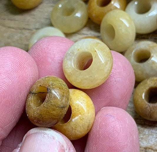 The yellow quartz beads in the close-up appear to have a vibrant, sunny yellow color with a smooth, polished surface. Each bead is approximately 5/8 inch in size, showcasing a translucent quality that allows light to pass through, creating a subtle glow. The hand holding the beads adds a human touch to the image, emphasizing their size and providing a sense of scale