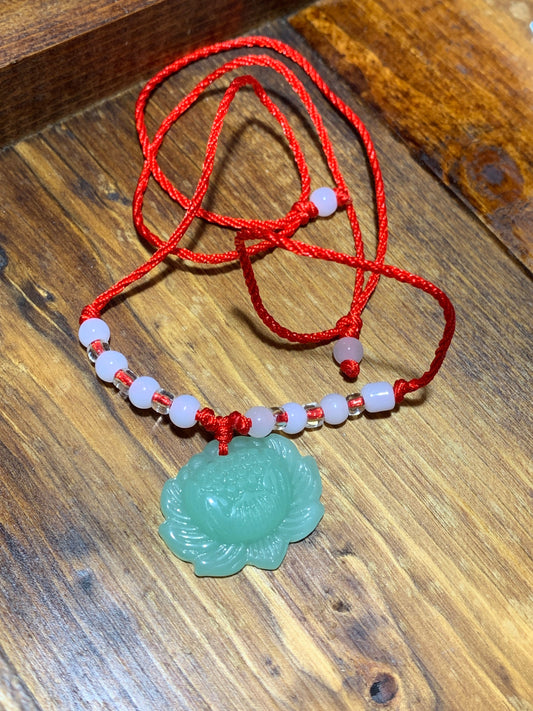 This playful jade lotus crystal pendant is attatched to a red cord with 4 white beads on either side.