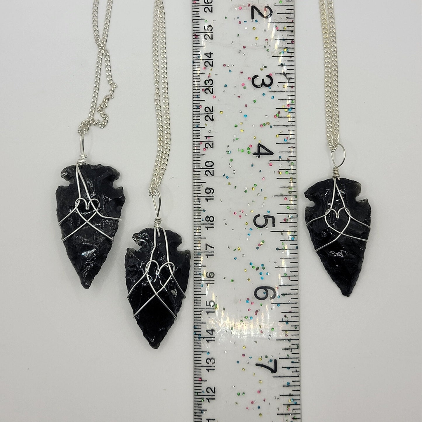 black obsidian 1 1/2" arrowhead, silver wire wrapped, handmade, pendant attarched to a silver chain, displayed next to a ruler