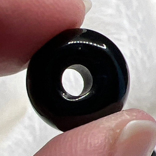 "Close-up view of a smooth, polished black obsidian bead, exhibiting a glossy surface with hints of reflected light.