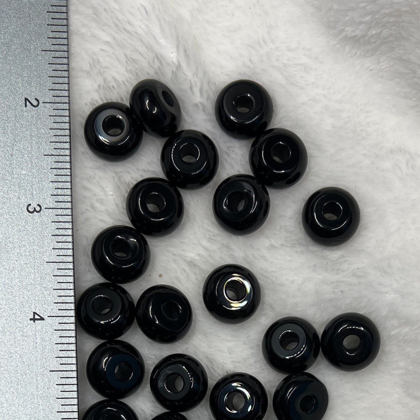 "Close-up view of a smooth, polished black obsidian beads, exhibiting a glossy surface with hints of reflected light, positioned next to a ruler to show size