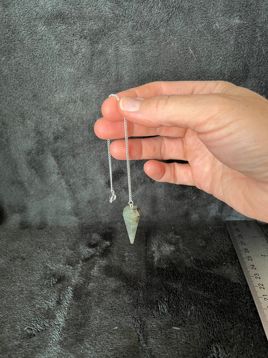 1 1/2 inch Labradorite crystal point pendulum attatched to an 8 inch silve chain, held dangling by a hand