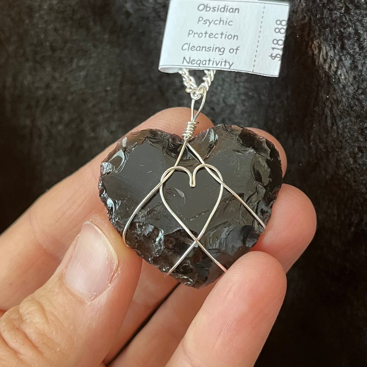 Silver wire wrapped obsidian knapped heart pendant, approximately 1" long, attatched to a silver chain. the wore wrapping makes a heart shape in the the middle of the obsidian heart crystal.