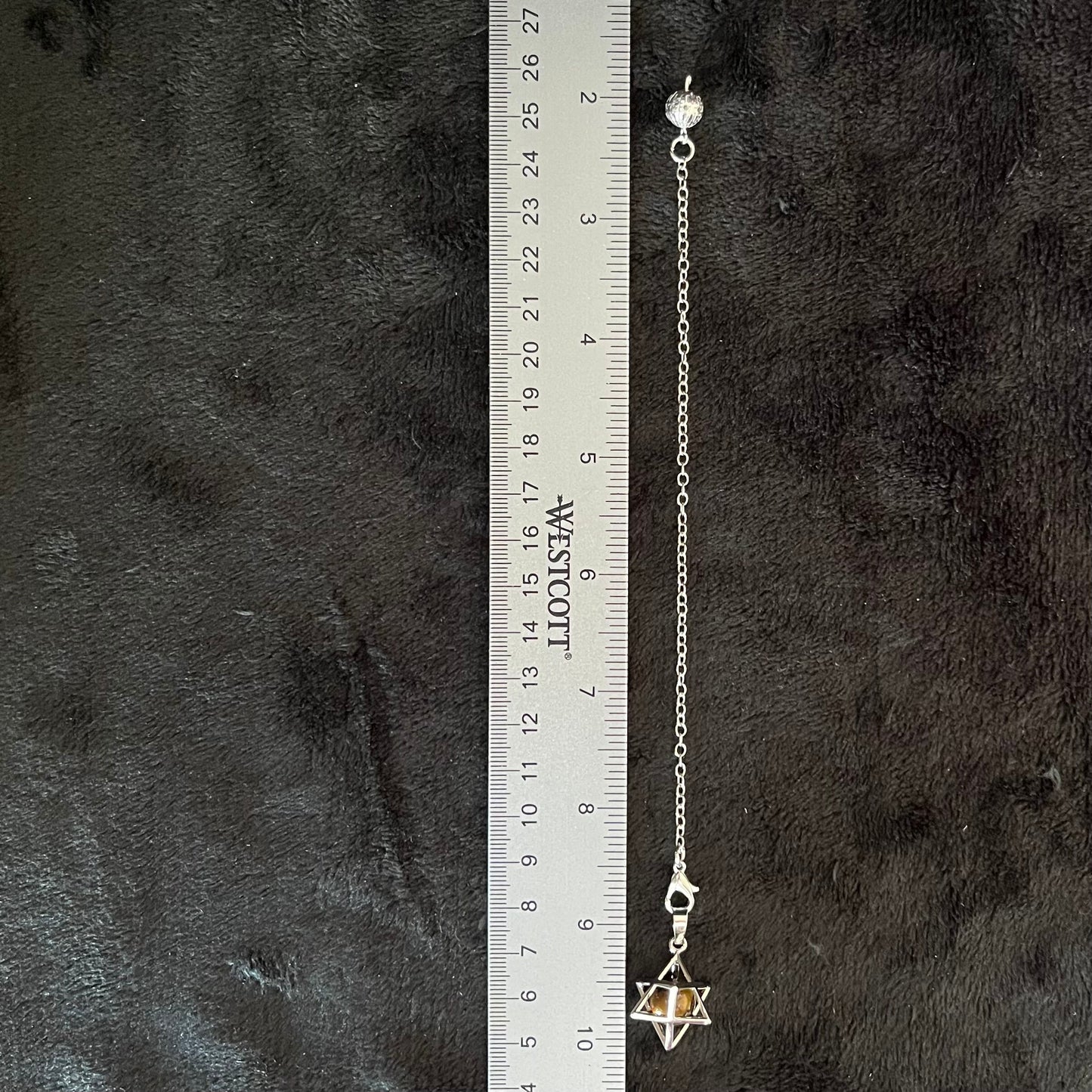 close up of a 1 cm shiny bronze and brown tigere eye sphere in a 1/2 inch sliver merkaba attatched to a 9 inch silver chain displayed next ro a ruler