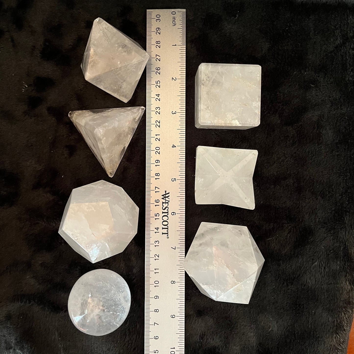Seven-piece sacred geometry quartz set featuring intricate patterns and precision-cut designs for spiritual and aesthetic significance, displayed next to a ruler. Each piece is 1 3/4” - 2 1/4” in diameter