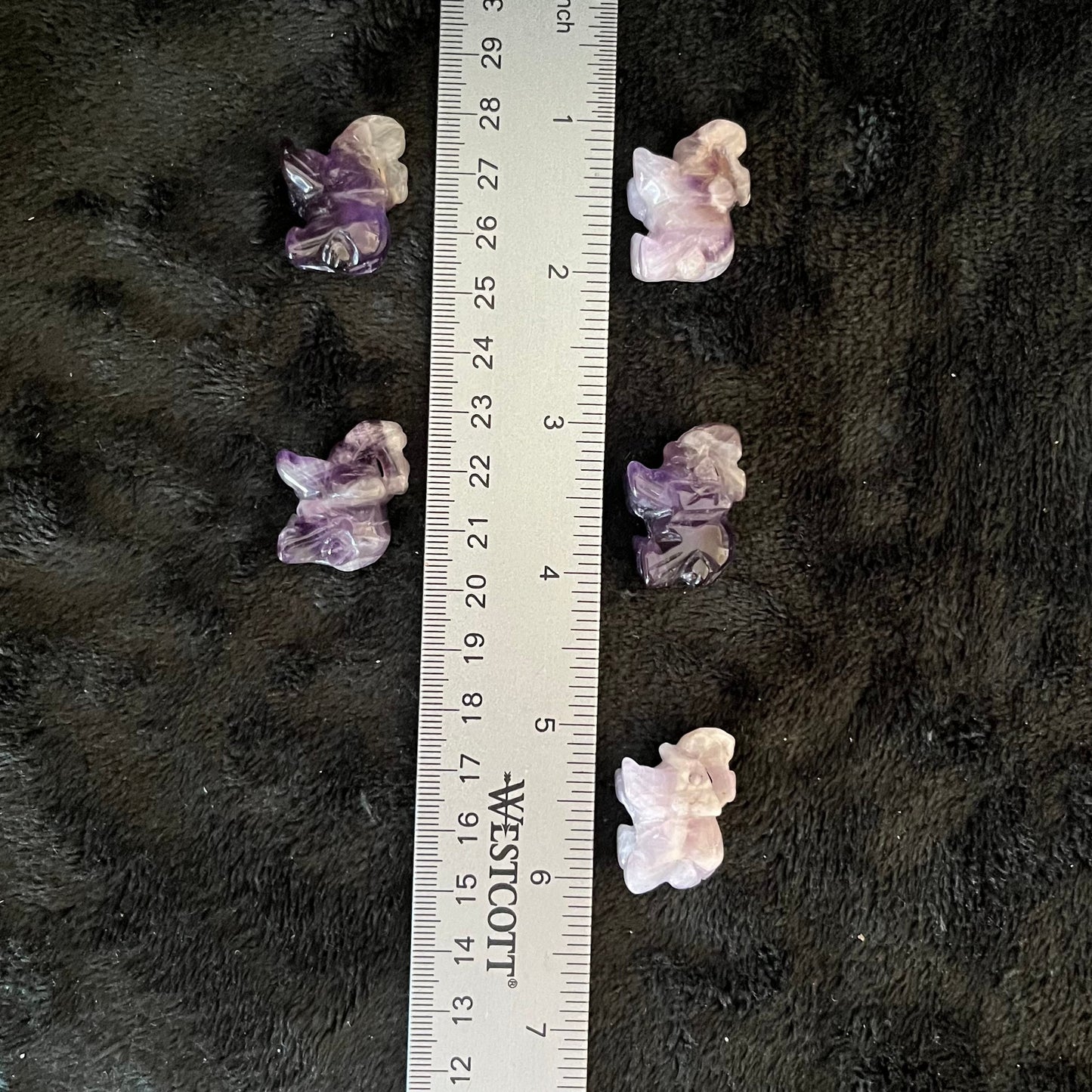 Small amethyst elephant carvings, showcasing intricately detailed craftsmanship and rich purple tones, displayed next to a ruler to show size. Amethyst elephants are approximately 1” x 3/4”.