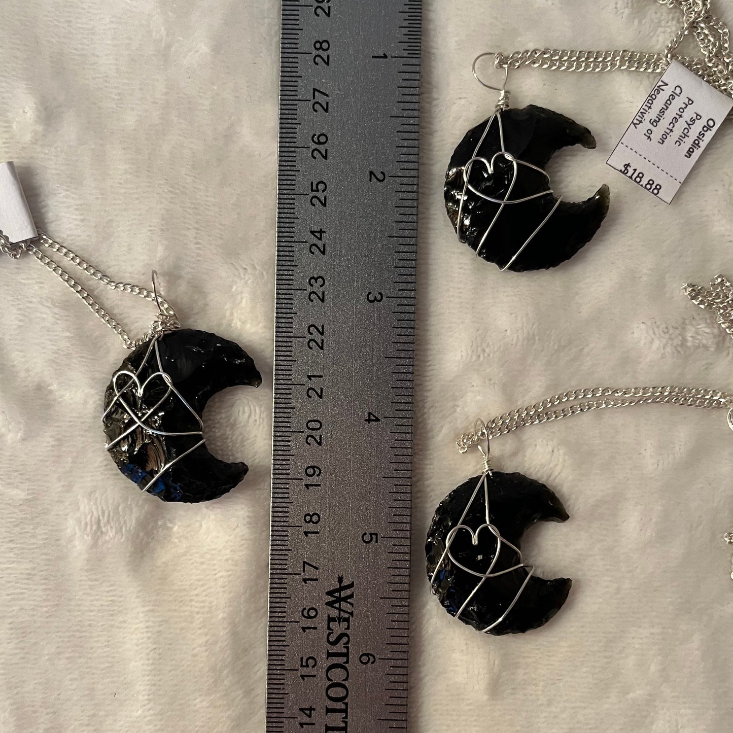 3 Silver wire wrapped obsidian crescent moon pendants with silver chains, diplayed next to a ruler to show size. Obsidian crystal moons are approximately 1 1/4" long