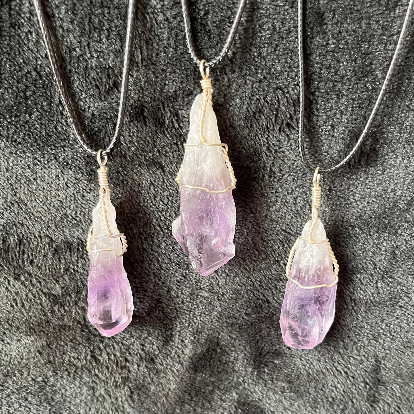 3 dragon tooth amethyst, silver wire wrapped pendants atrercued to adjistable black cords displayed against a black backgeound to luminate the whote and translucent purple colors.