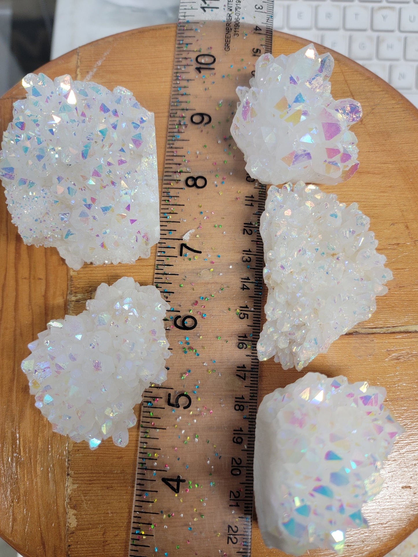 "Angel aura quartz cluster with iridescent rainbow colors, reflecting light and promoting a sense of peace and serenity, displayed next to a ruler. crystals are 2" - 3" long