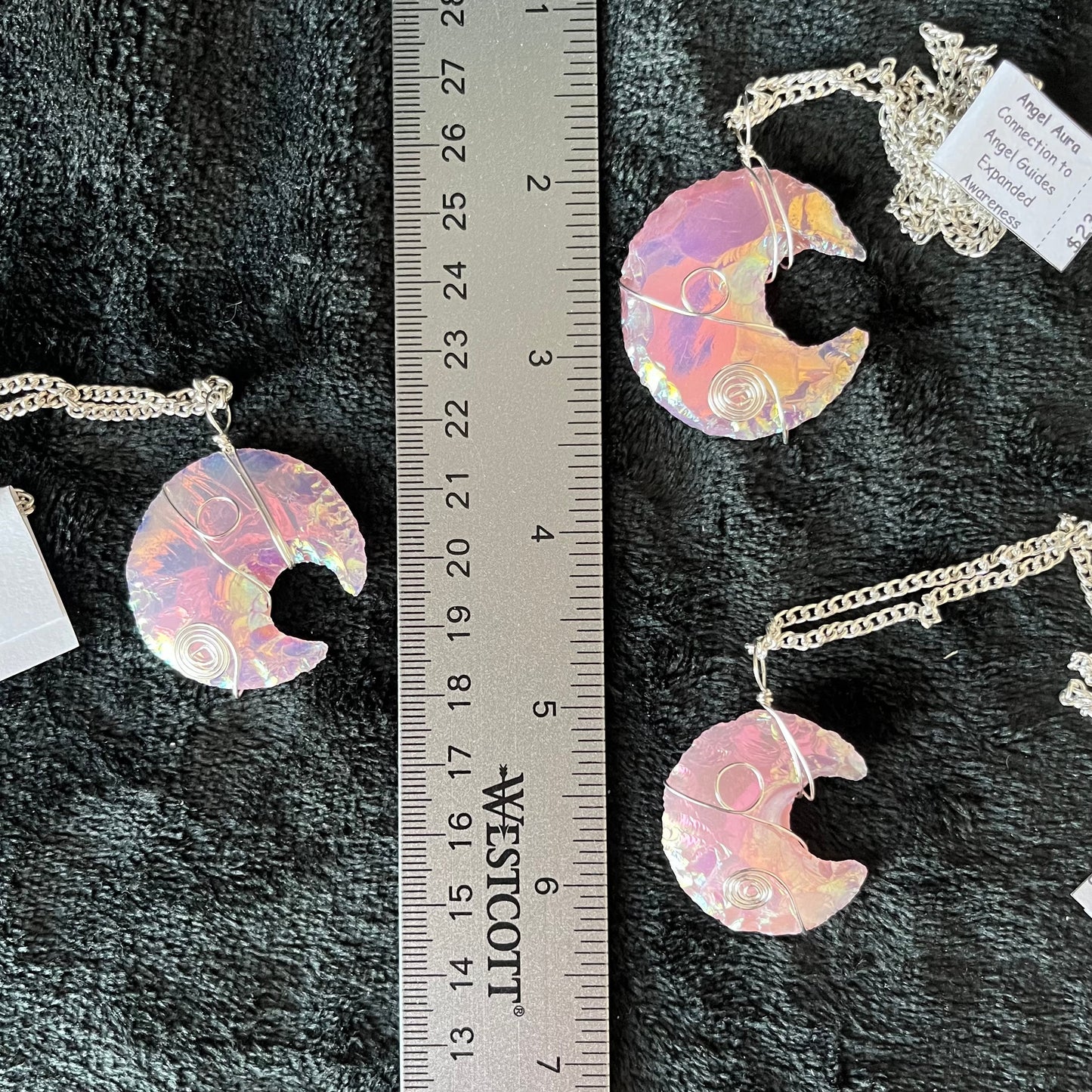 shimmery mettallic lookong ponk angel aura pink opalite, knappes creacent moon ornately silver wire wrapped pendant attatched to a silver chain, next to a ruler