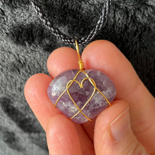 close up of 1 inch purple and white amethyst heart, gold wire wrapped pnedant attached to a black cord