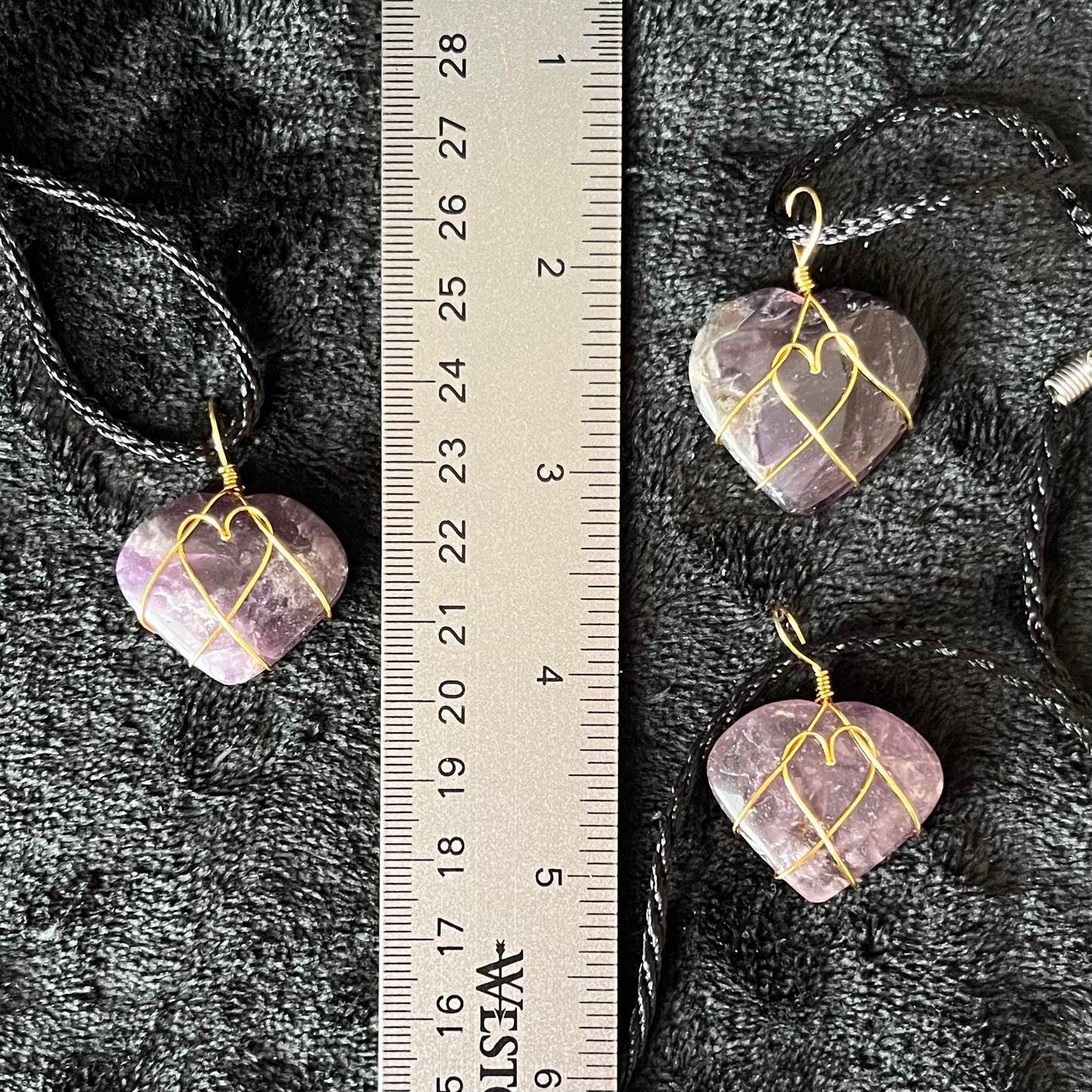 close up of 1 inch purple and white amethyst heart, gold wire wrapped pnedant attached to a black cord, displayed next to a ruler