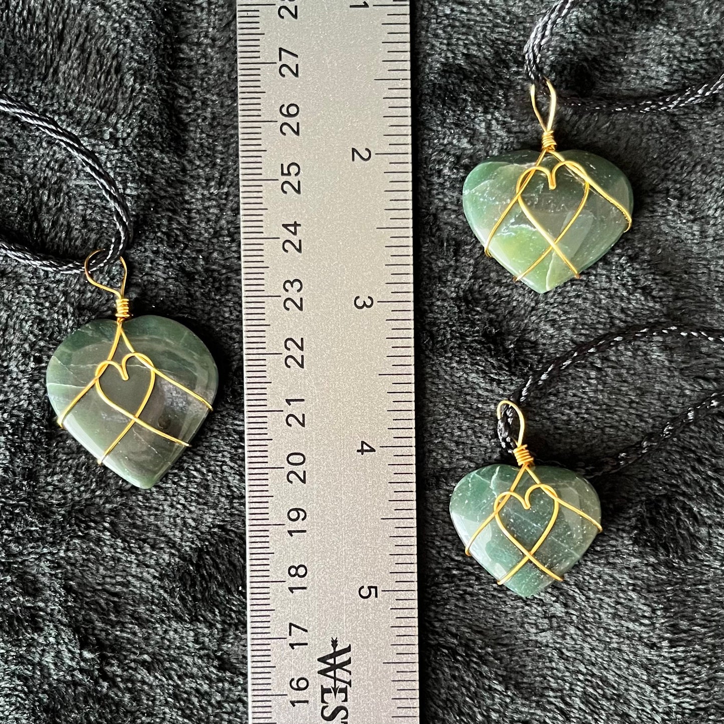 3 Gold wire wrapped, green jade heart pendants, approximately 3/4" X 1", attarched to adjustable black cords, displayed next to a ruler.