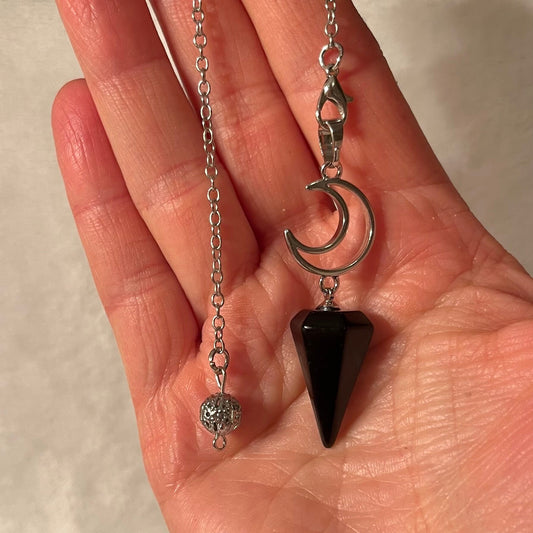 1 inch black obsidian pendulum attarched to a silver crescent moon, both connected to an 8 inch silver chain displayed delicately in the palm of a hand