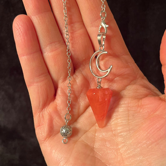 1 inch cherry quartz pendulum attatched to an 8 inch silver chain including a silver crescent moon displayed in the palm of a hand