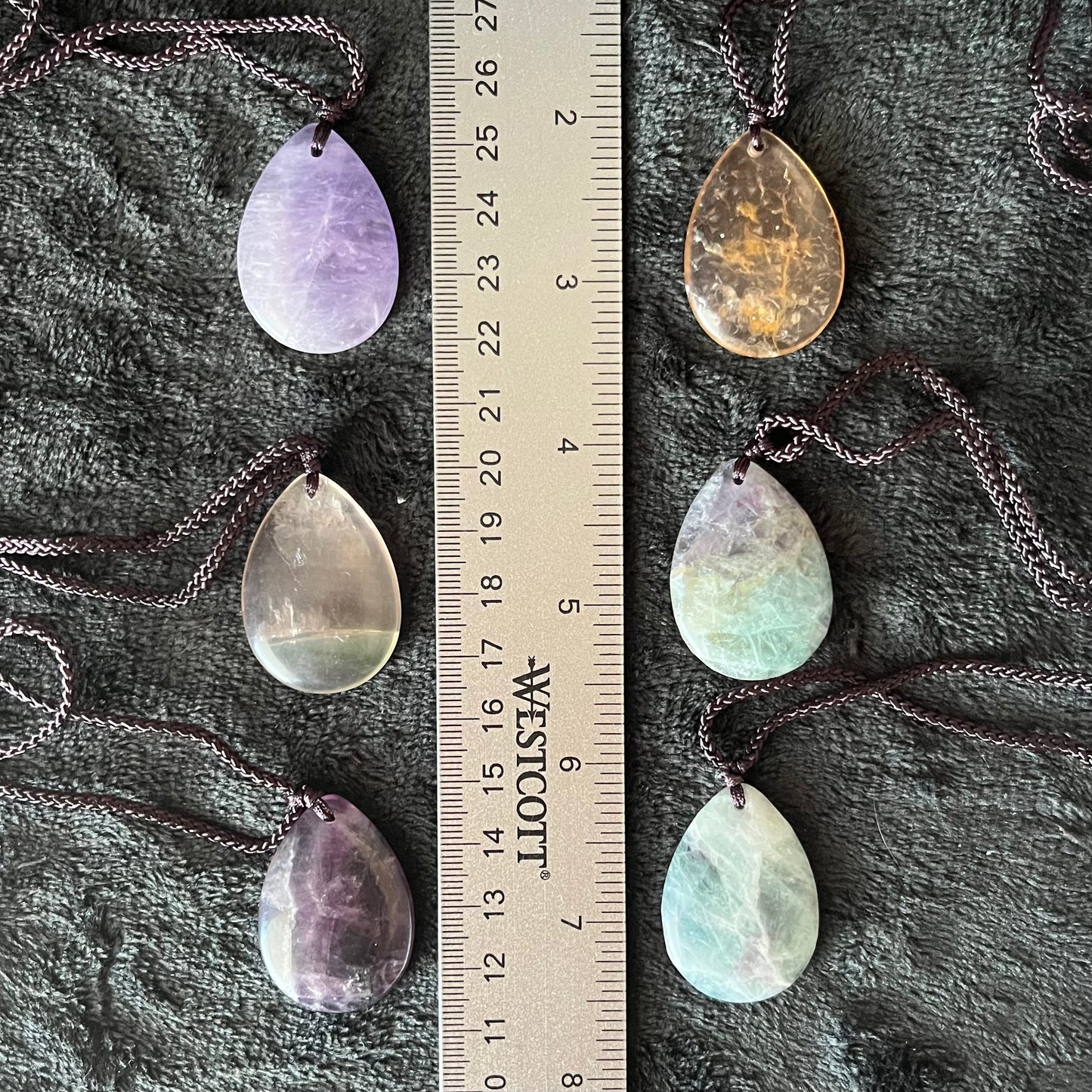 6 Captivating fluorite teardrop pendant necklaces, elegantly suspended from delicate adjustable black cords, crystal pendants are approximately 1 1/4” long.