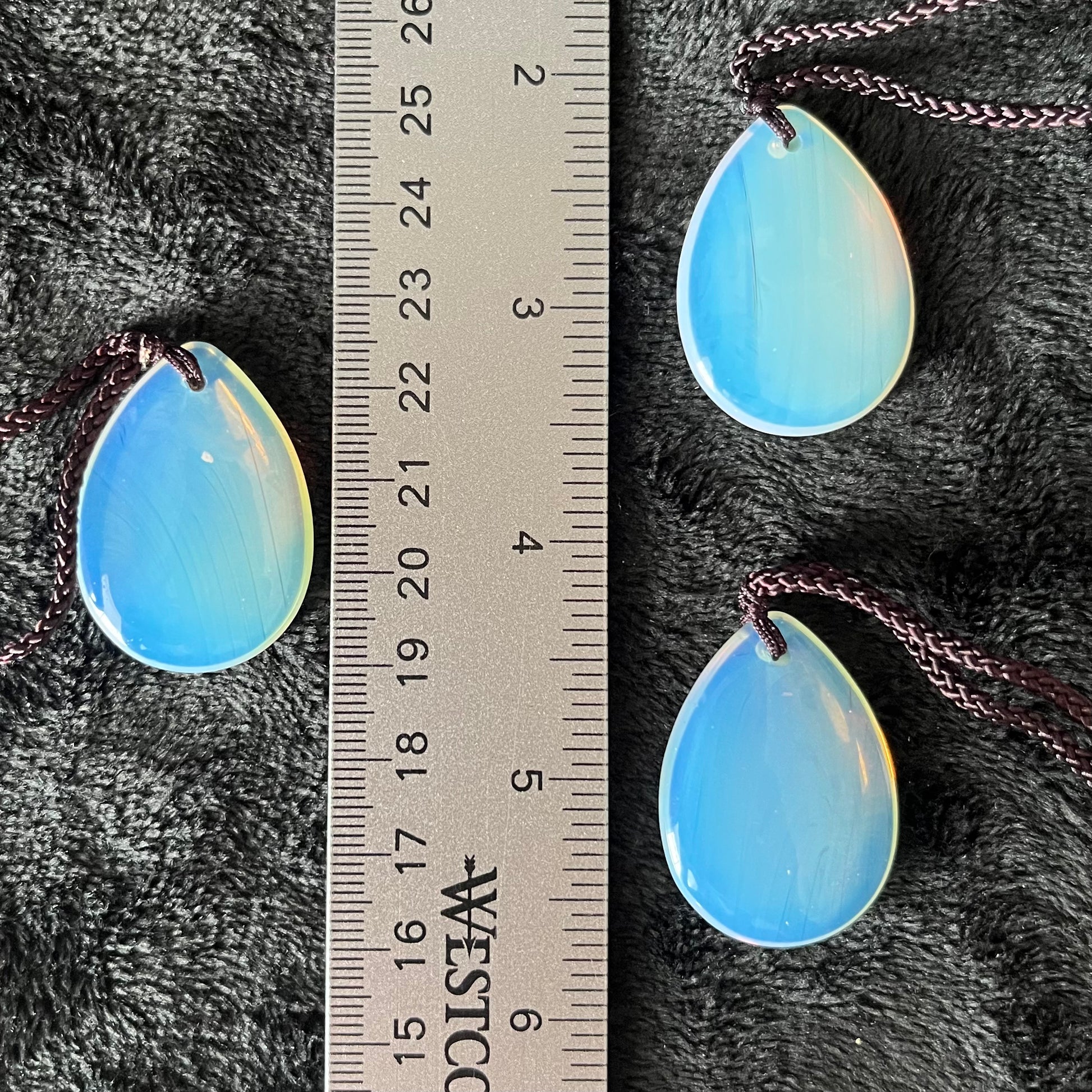 Iridescent opalite teardrop pendant suspended from a delicate adjustable brown cord, displayed next to a ruler to show size.  Crystal pendant is approximately 1 1/4” long