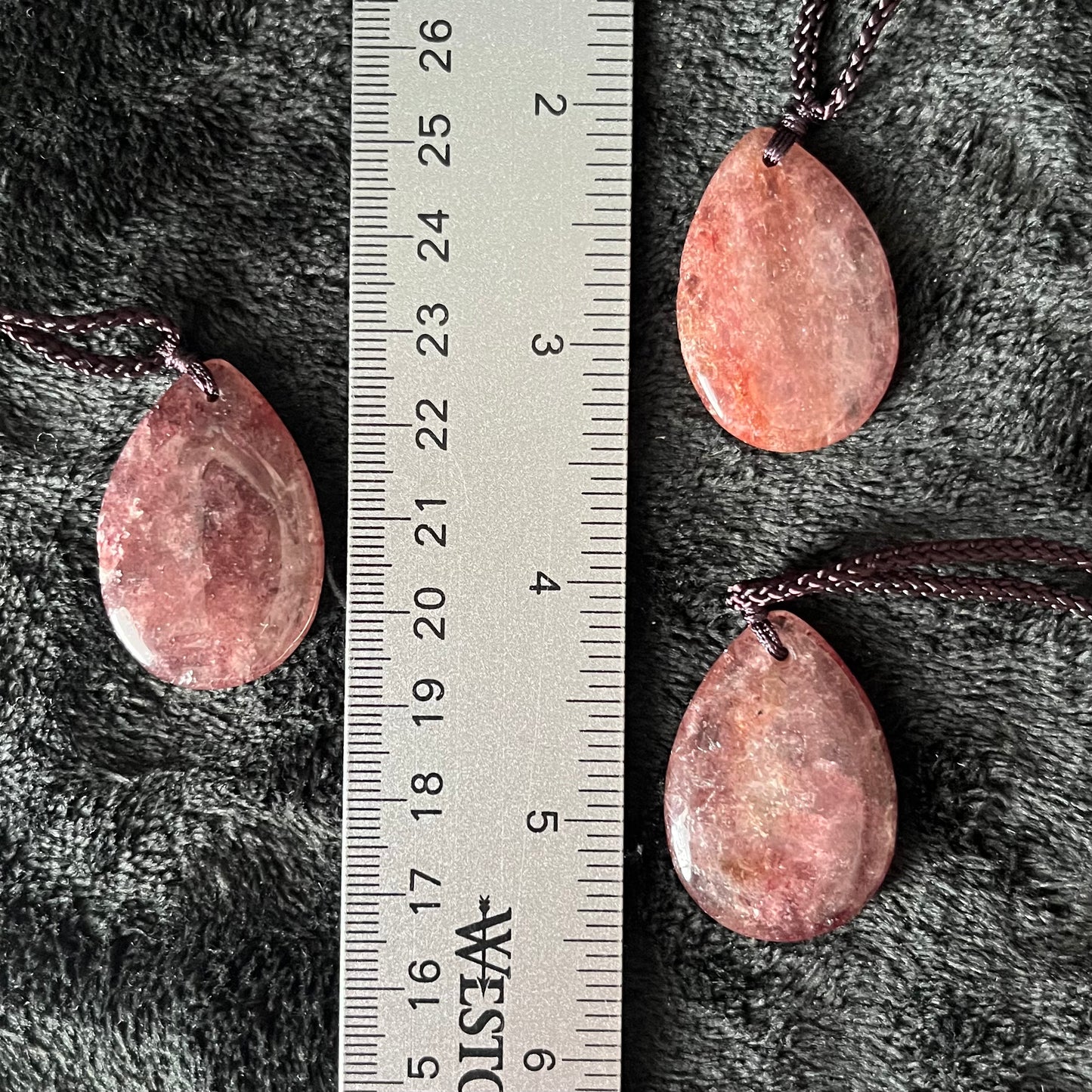 Radiant strawberry quartz teardrop pendant necklace, showcasing a sweet blend of pink hues in a captivating gemstone, elegantly suspended from an adjustable cord displayed next to a ruler.  Crystal pendant is approximately 1 1/4” long