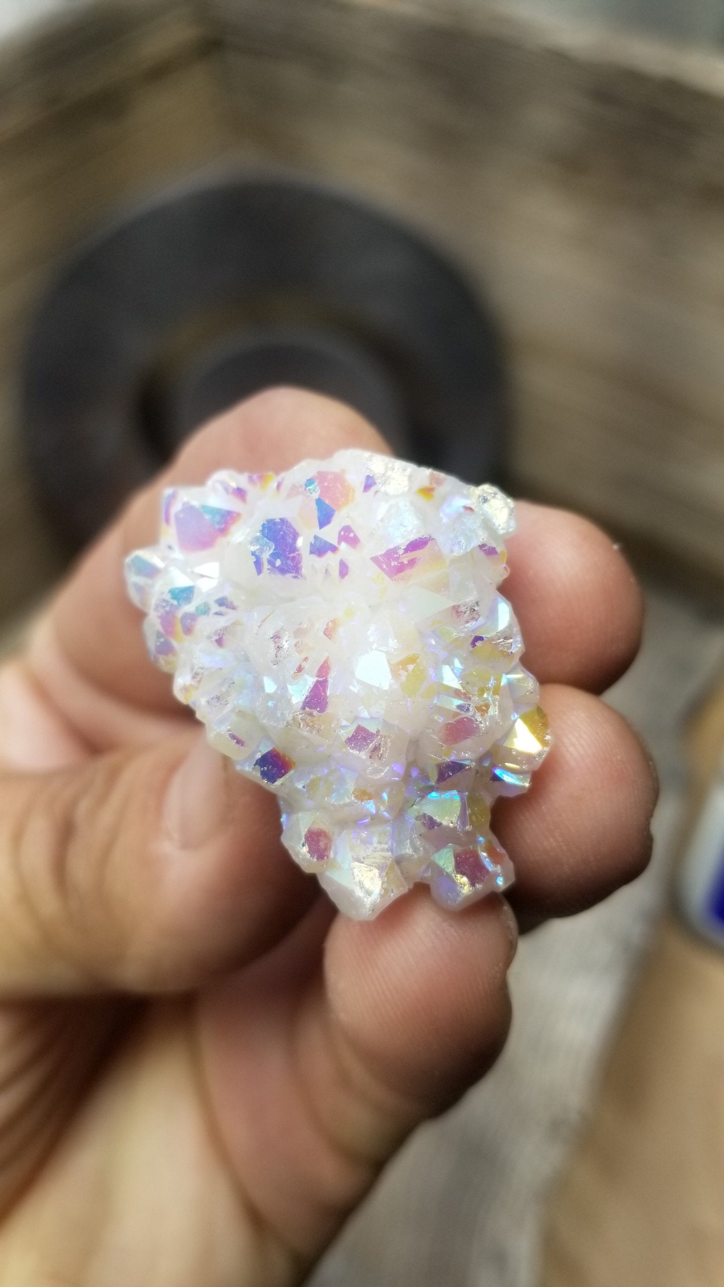 "Angel aura quartz cluster with iridescent rainbow colors, reflecting light and promoting a sense of peace and serenity.  this small quartz clister is delicately held by fingertips