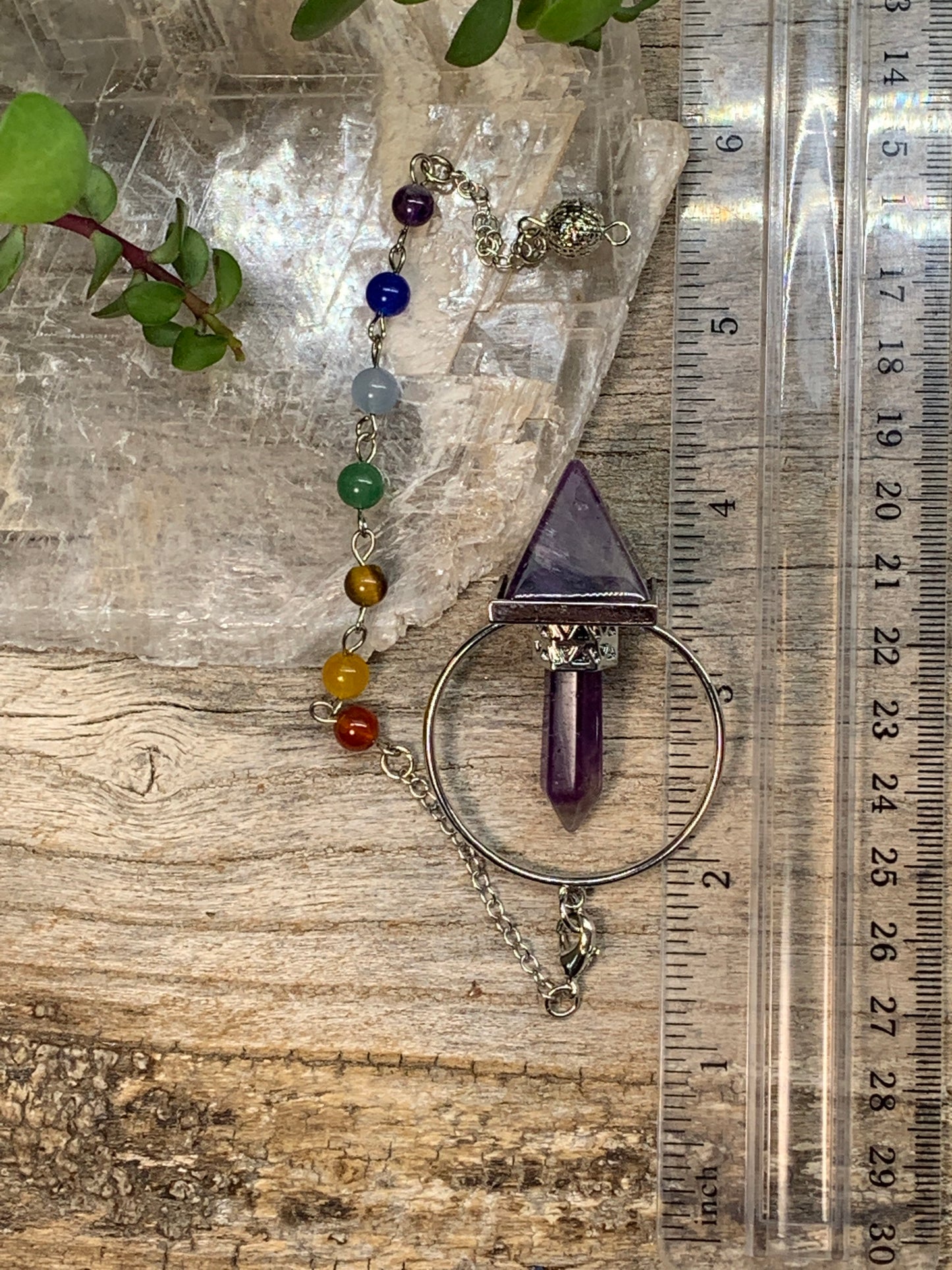 2 inch amethyst pendulum including an inverted amethyst pyramid attatched to an amethyst crystal in a silver ring, suspended from an 8 inch silver chain including chakra beads, displayed next to a ruler