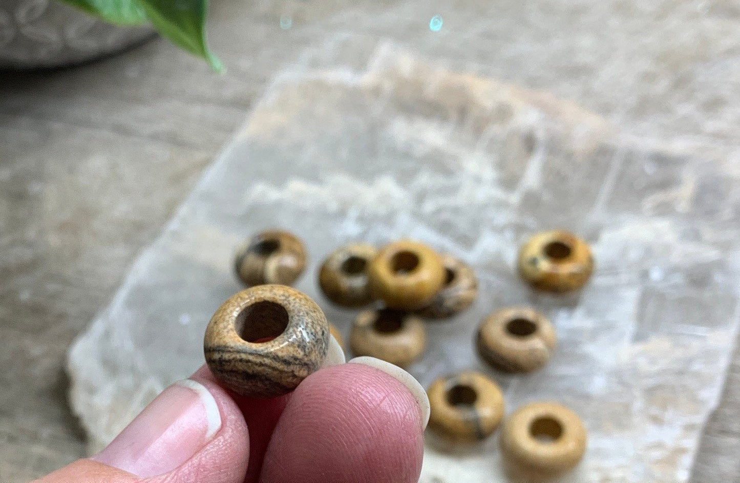 Image of polished Jasper beads, each measuring 5mm in diameter. The beads display a mix of earthy tones, including browns, yellows, and greys, with unique patterns and swirls