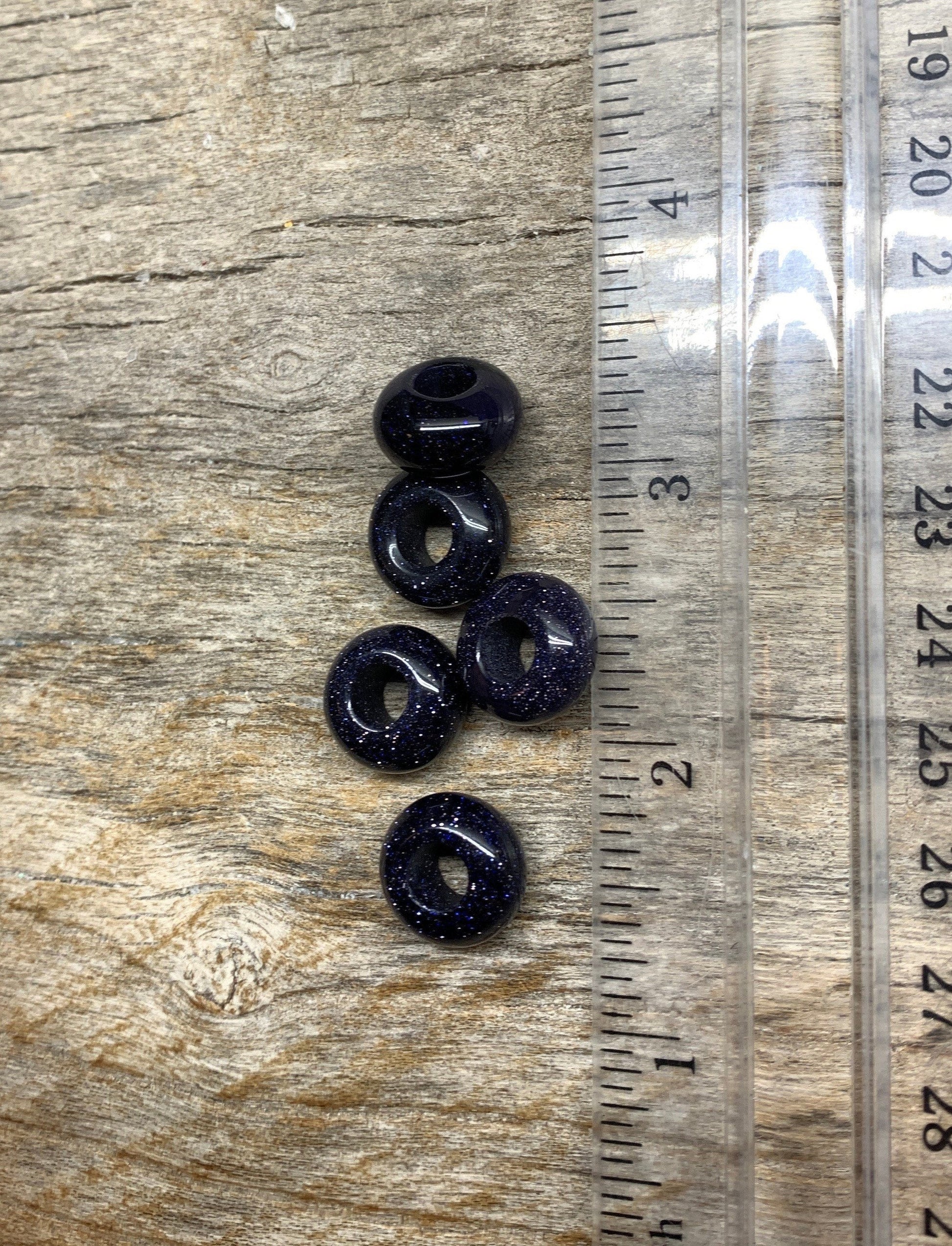 "Five blue goldstone beads, each measuring 5mm in diameter. The beads exhibit a deep blue color with sparkling metallic flecks, creating a captivating and shimmering appearance, positioned next to a ruler