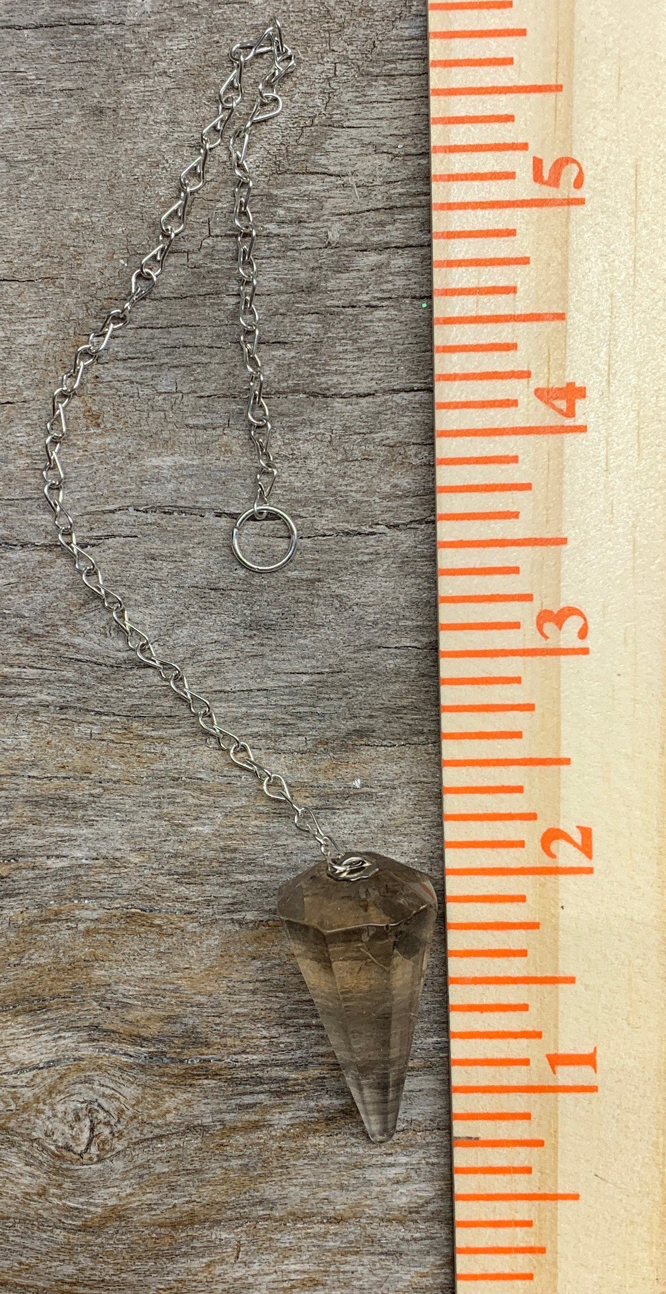 1 1/4 inch smoky quartz crystal point pendulum including a silver 8 inch chain displayed next to a ruler