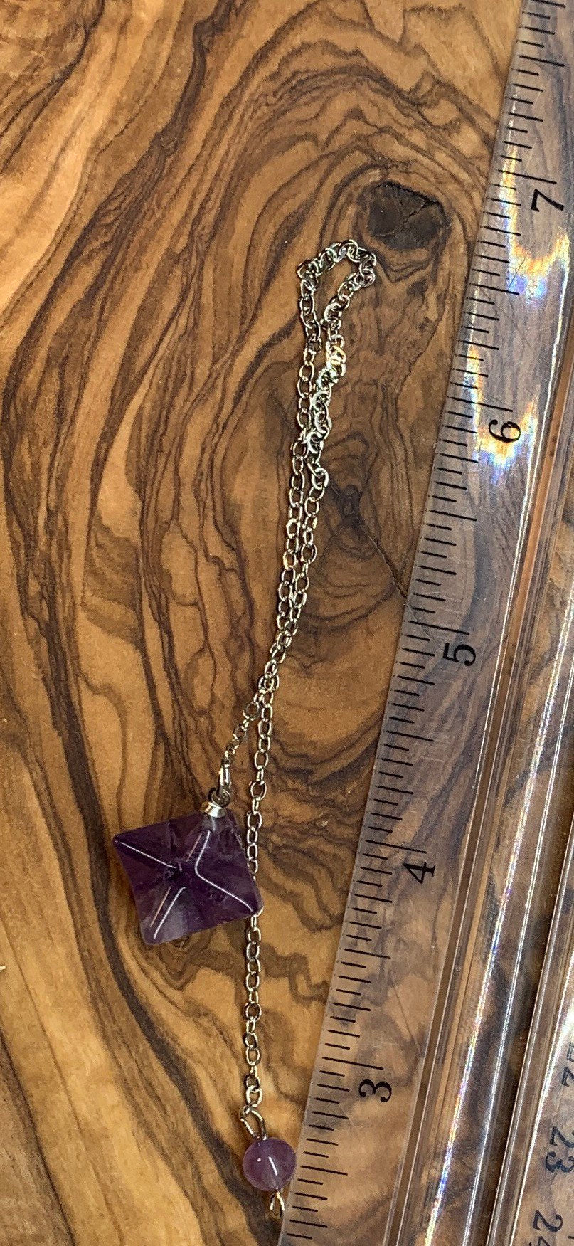 3/4 inch amethyst merkaba pendulum attatched to an 8 inch silver chain displayed next to a ruler