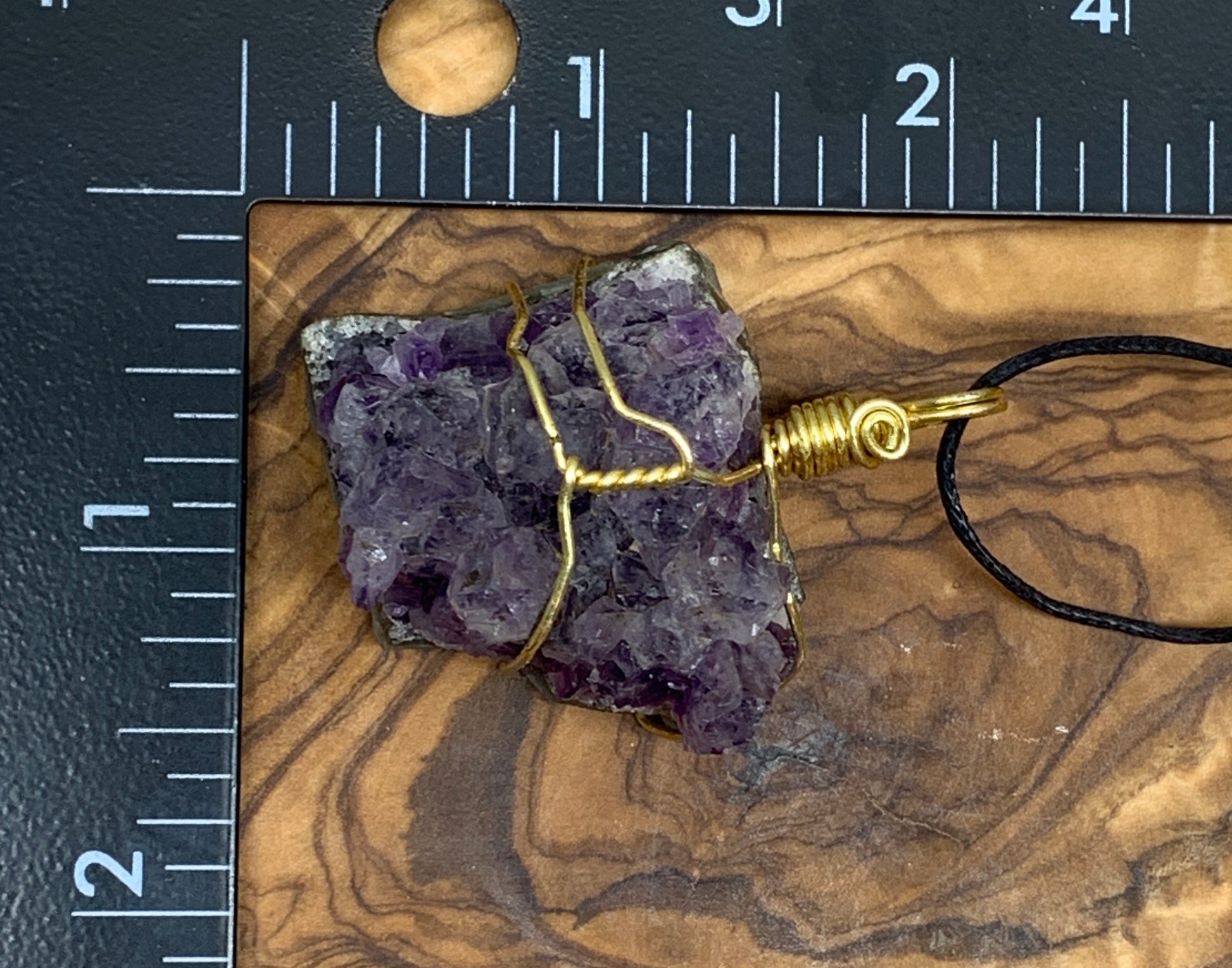 Wire-wrapped necklace adorned with a small amethyst cluster, beautifully showcasing the natural crystal formations, display next to a relaxe.