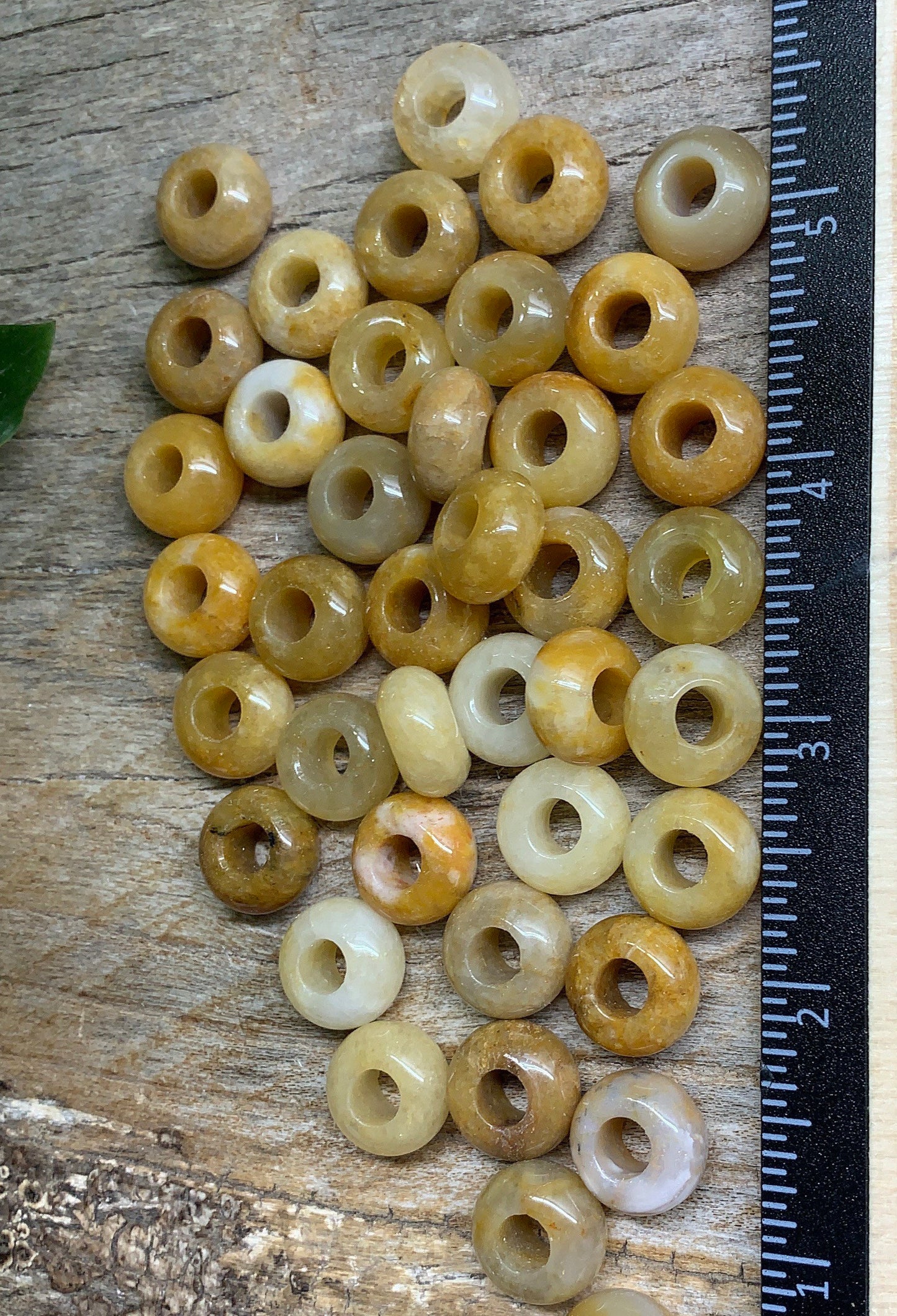 The yellow quartz beads are characterized by their bright and cheerful yellow hue. They exhibit a glossy, polished surface that reflects light, enhancing their vibrancy. The arrangement of the beads next to the ruler allows you to gauge their size, indicating that they vary in diameter and are likely uniform in shape. The ruler serves as a visual reference point for the size of these beads.