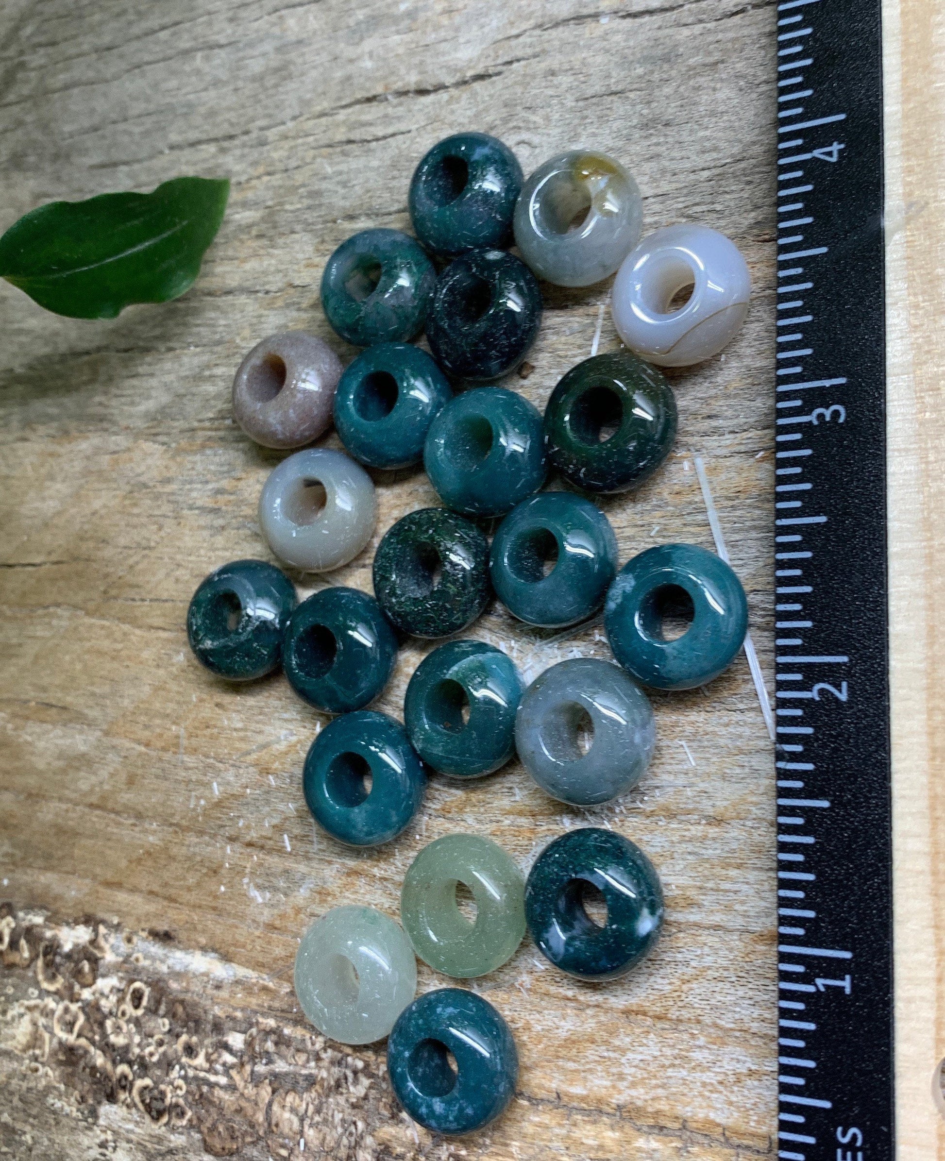 "Close-up view of lustrous moss agate beads, showcasing intricate green and brown patterns, next to a ruler to show size of 5/8"