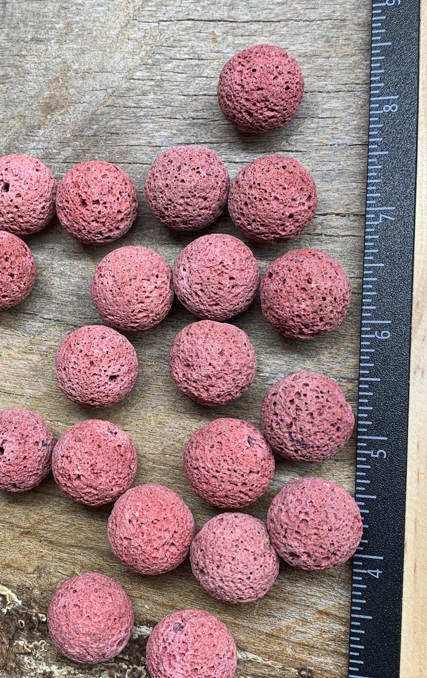 "Close-up of round pink lava beads, showcasing their textured surface and vibrant color, positioned next to a ruler to show size.