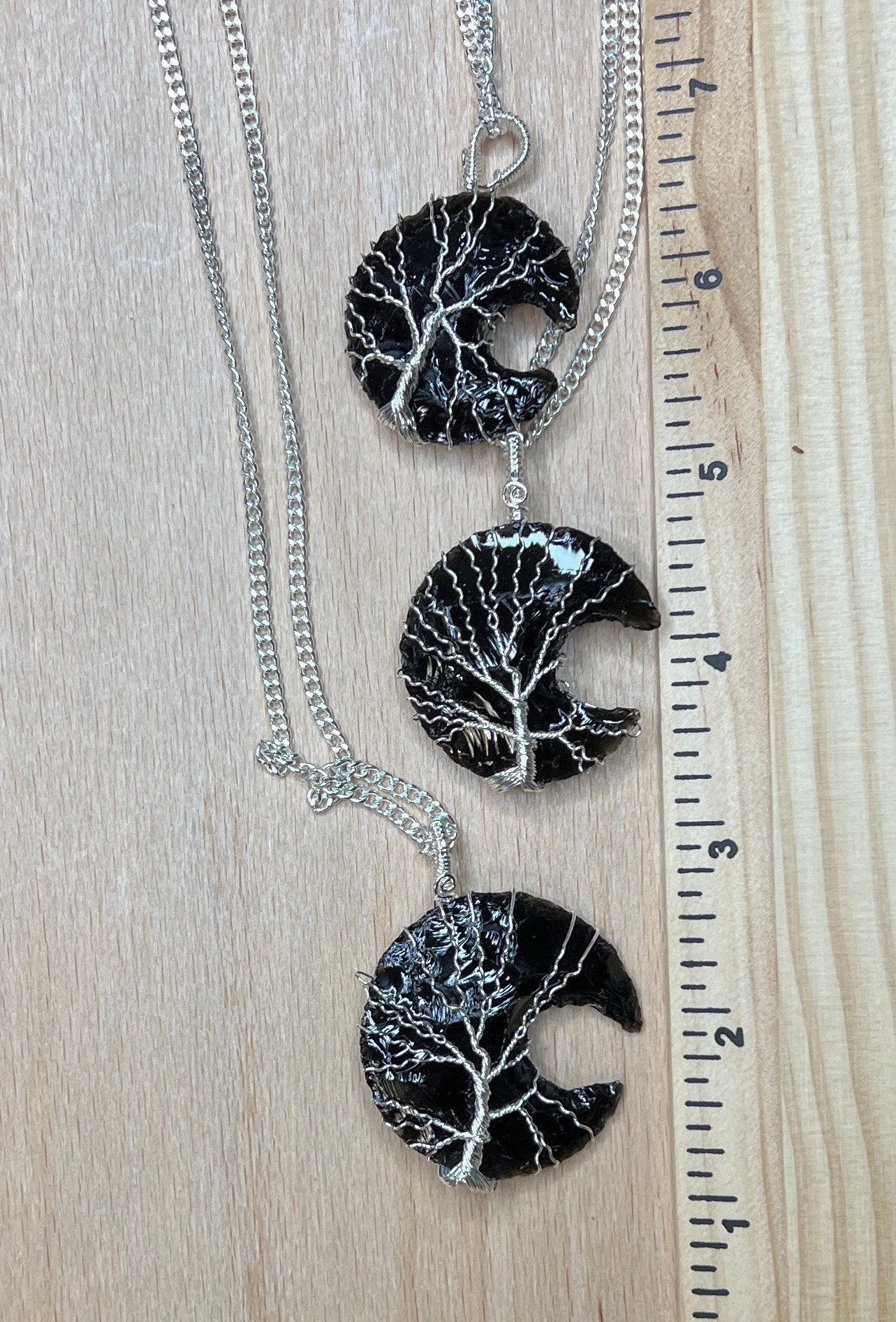 3 Tree of Life Silver wire wrapped obsidian crystal crescent moon pendants with silver chains, displayed next to a ruler.  obsidian crustal moons are 1 1/4" - 1 1/2" long