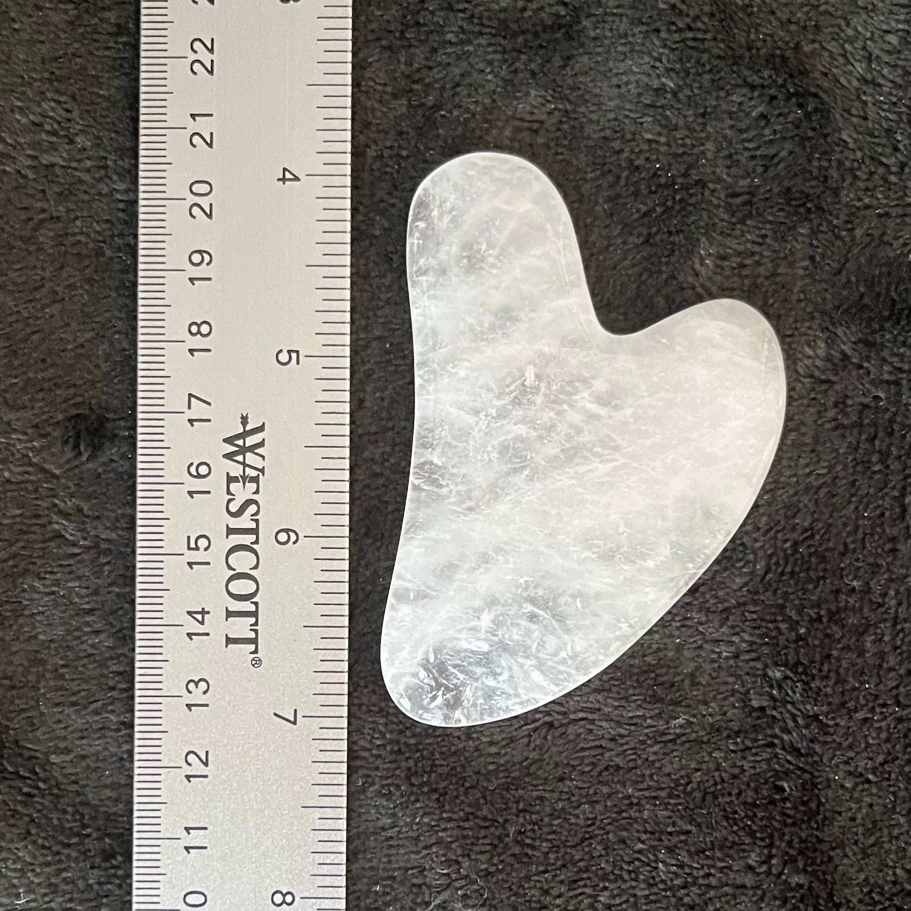 "Quartz Guasha stone featuring a smooth, clear surface, perfect for facial massage and skincare routines, display next to a ruler to show size. Quartz Quasha stone is approximately 3 inches long.