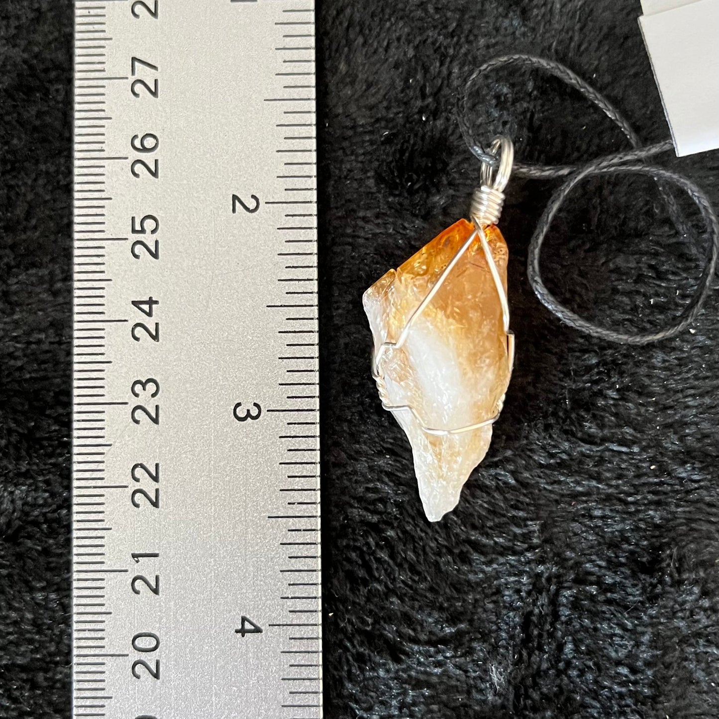 golden yellow translucent citrine crystal, solver wire wrapped  and attatched to an adjistable black cord, displayed next to a ruler.  pendant is approximately 1 inch long.