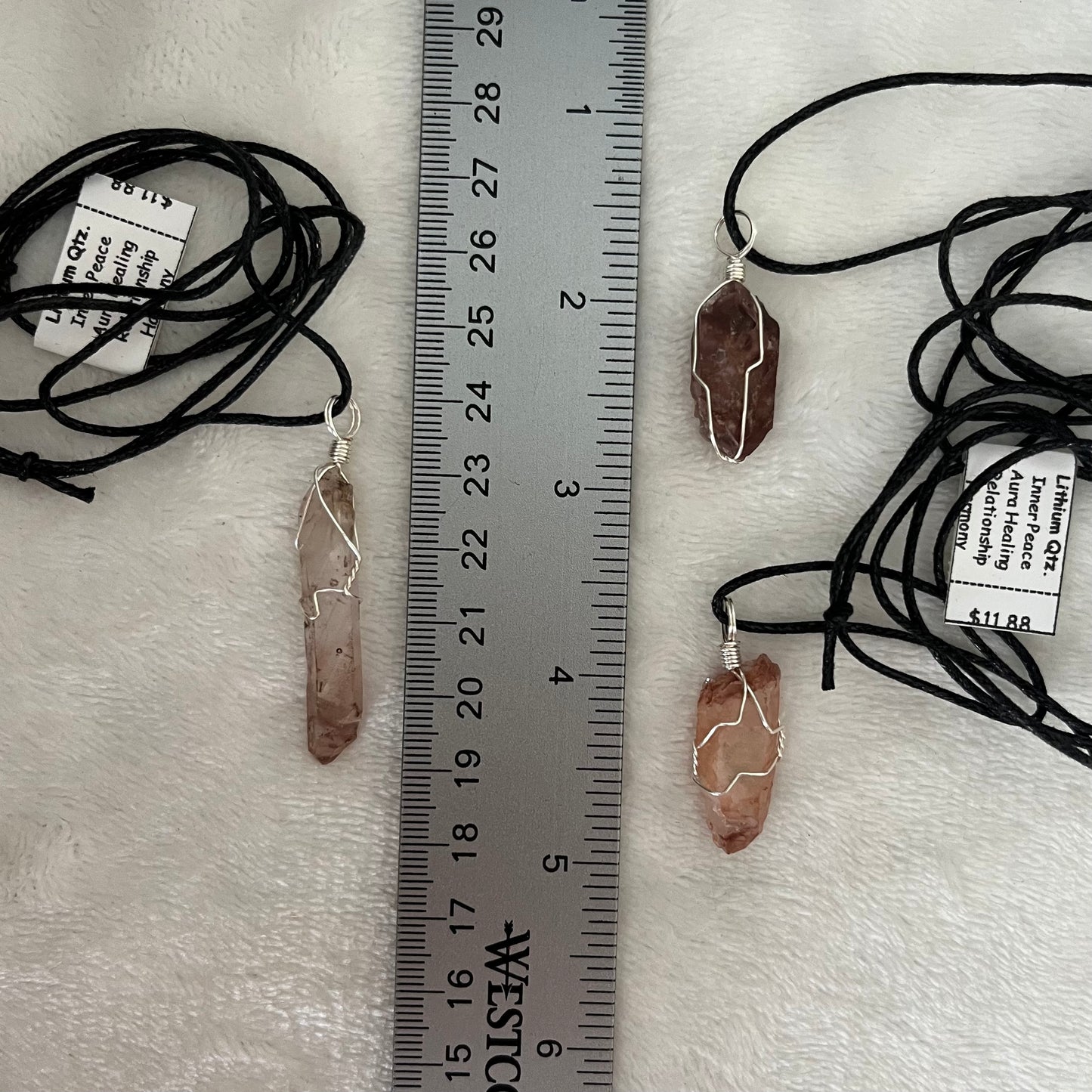 3 ornately silver wire wrapped lithium quartz pendants varying im color from clear to orange to red, including black cords displayed against a white background next to a ruler