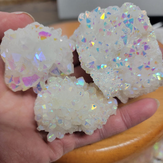 "Angel aura quartz cluster with iridescent rainbow colors, reflecting light and promoting a sense of peace and serenity, held in one hand