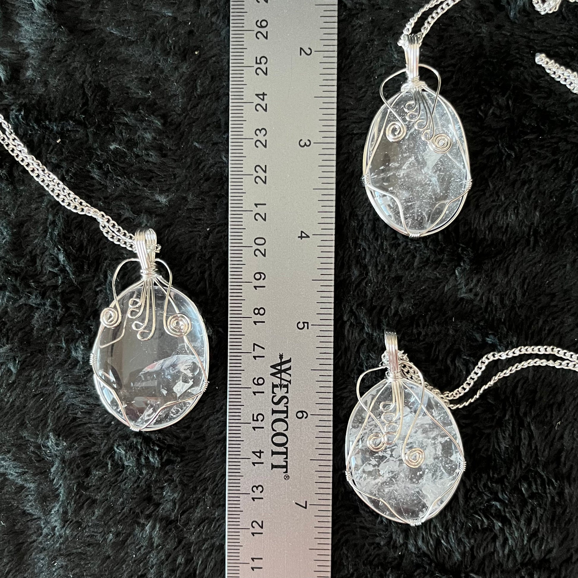 Three silver fancy wire wrapped clear quartz oval stone pendants attatched to silver chains, displayed next to a ruler.  quartz ovals are 1 3/4" - 2 1/4" long