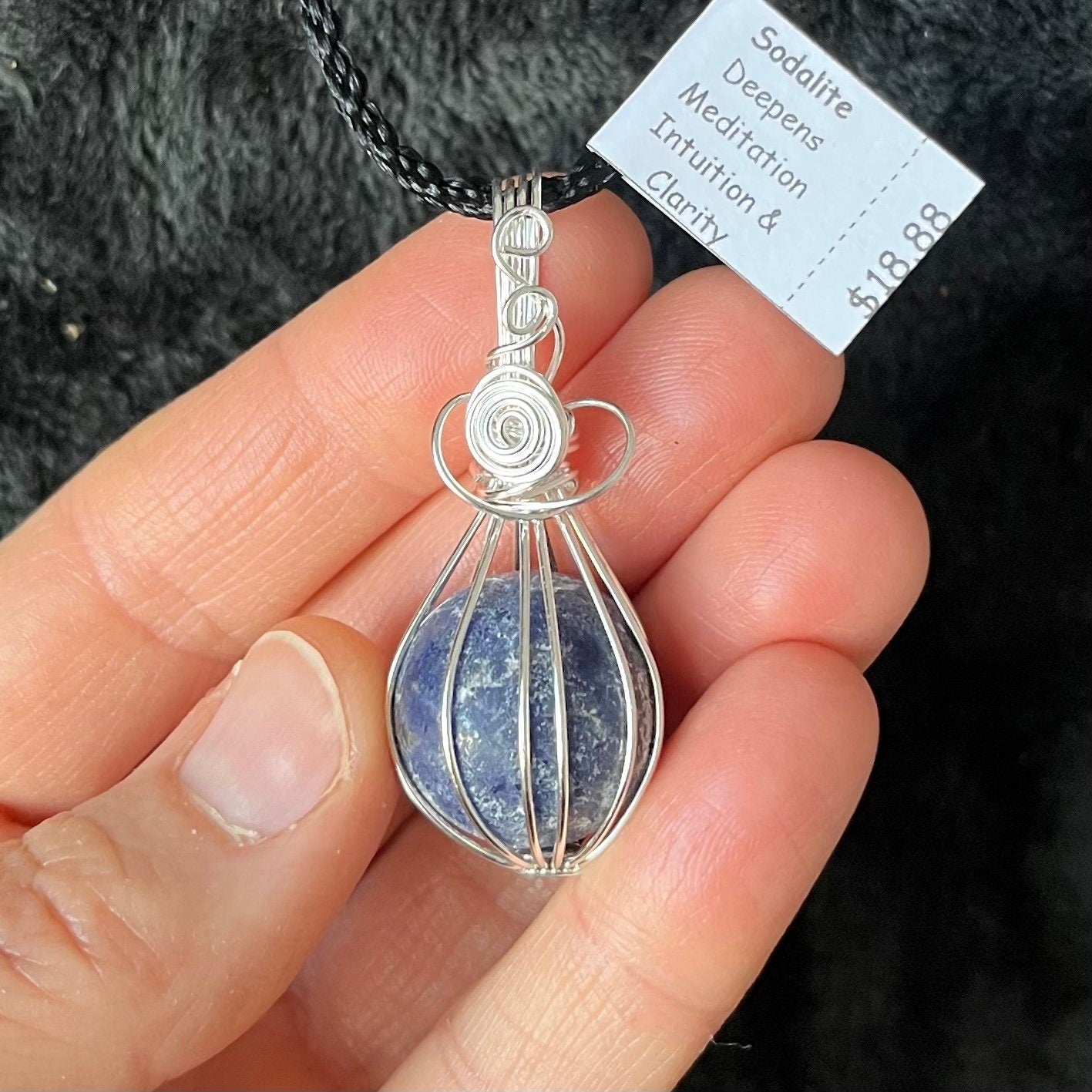 Ornately silver wire wrapped basket pendant containing a blue amd grey sodalite sphere approximately 1/2" in diameter amd attatched to a black cord.