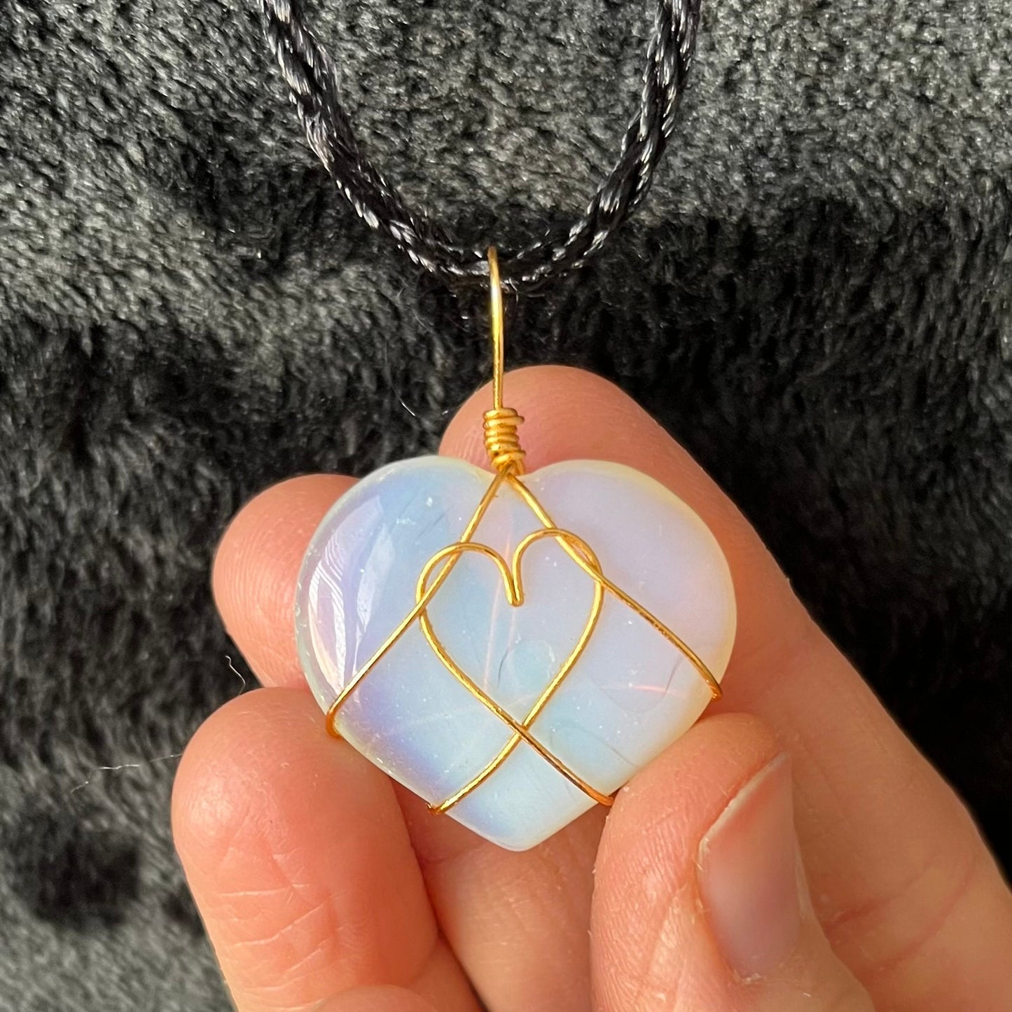 gold wire wrapped transluscent white opalite heart pendant, approximately 1" long, attatched at a black cord. 