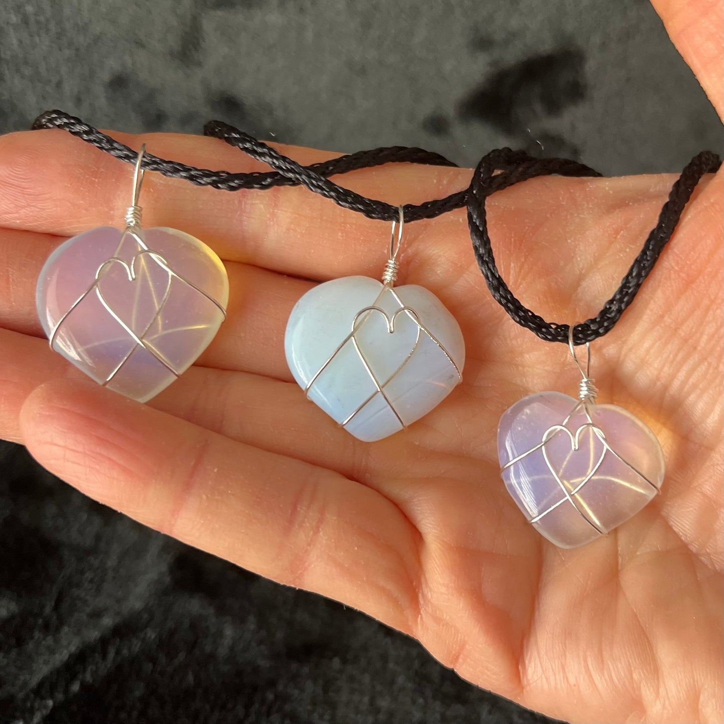 3 silver wire wrapped transluscent white opalite heart pendants approximately 1" long, attatched at a black cords, displayed next to a ruler.