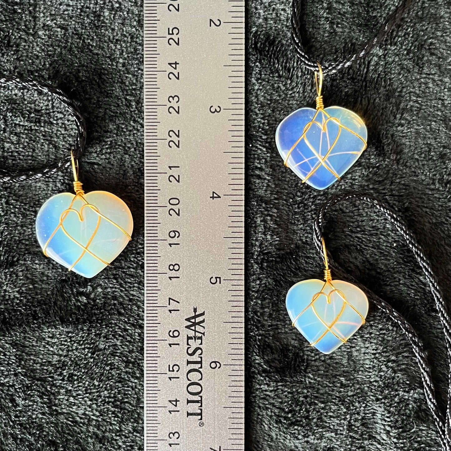 3 gold wire wrapped transluscent white opalite heart pendants, approximately 1" long, attatched at a black cord, displayed next to a ruler