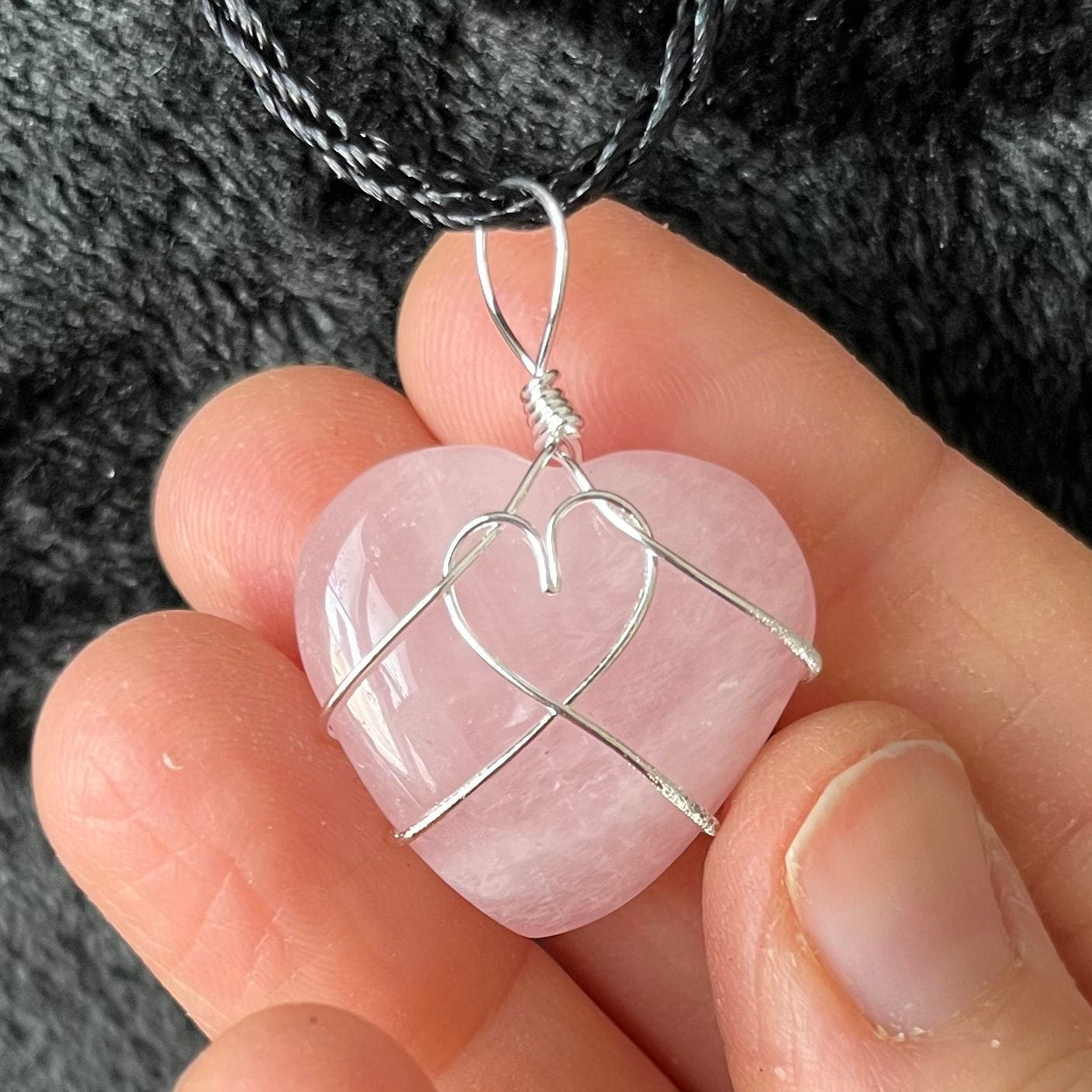Wire-wrapped rose quartz heart necklace: a silver wire intricately wraps around a polished rose quartz heart pendant, hanging on a delicate chain.  The wire makes a heart shape in the middle of the rose quartz heart.