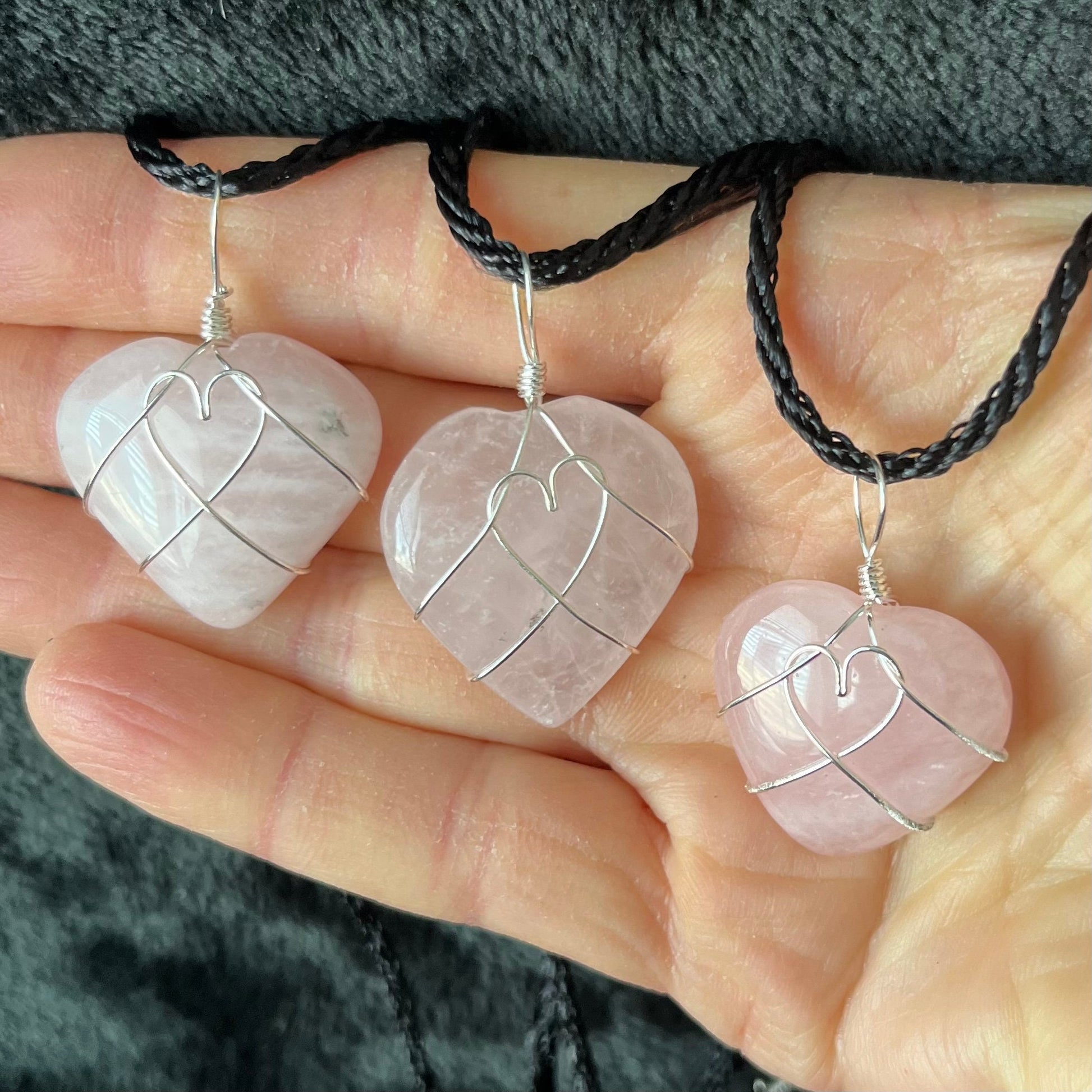 Three Wire-wrapped rose quartz heart necklaces: a silver wire intricately wraps around polished rose quartz heart pendants, hanging on a delicate chain.  The wire makes a heart shape in the middle of the rose quartz hearts.