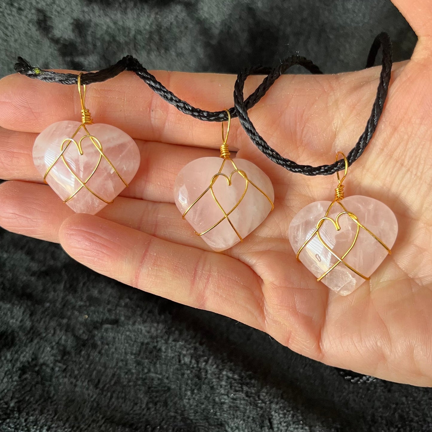 Three Wire-wrapped rose quartz heart necklaces: a gold wire intricately wraps around polished rose quartz heart pendants, hanging on a delicate chain.  The wire makes a heart shape in the middle of the rose quartz hearts.